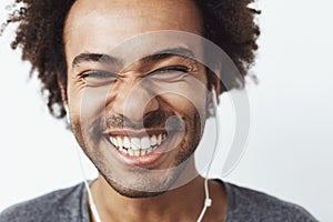 Close up portrait of young happy african man smiling listening to upbeat streaming music laughing over white background