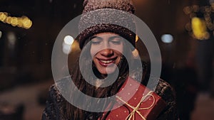 Close Up of Portrait of Young Happy Attractive Girl in Winter Hat and Mittens, Holding Present Box, Standing in Falling