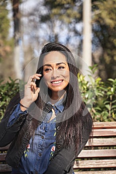 Close up portrait, young, happy beautiful woman, talking on cell phone, sitting on park bench, isolated outside outdoor