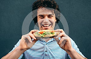 Close-up portrait of young happy man eating a healthy hamburger. Handsome man in a fast food restaurant eating a hamburger