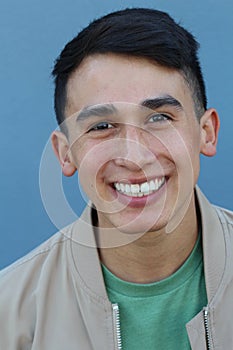 Close up portrait of a young hispanic teenager man looking at camera with a joyful smiling expression, against a blue background