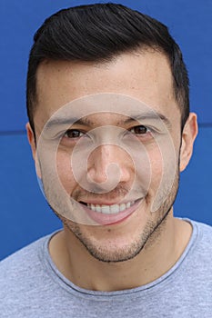 Close up portrait of a young Hispanic teenager man looking at camera with a joyful smiling expression, against a blue background