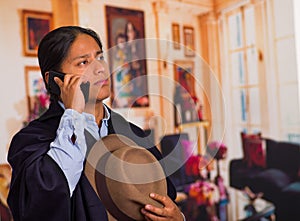 Close up portrait of young indigenous man wearing hat and poncho using cell phone