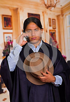 Close up portrait of young indigenous man wearing hat and poncho using cell phone