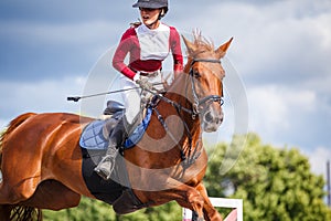 Close up portrait of young jockey girl leaping over obstacle on show jumping competition