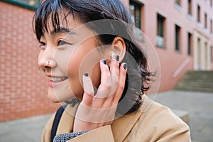 Close up portrait of young korean woman touches earphone, listens music in headphones with pleased smiling face, walks