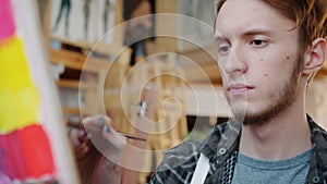 Close-up portrait of young man artist painting picture in studio looking at canvas