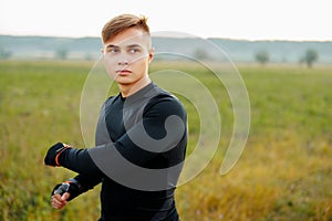 Close Up portrait, young man in black shirt, stretching arms, isolated green trees background. Warming up