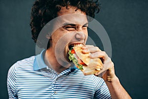 Close-up portrait of young man eating a cheeseburger has pleasant expression. Hungry man in a fast food restaurant eating a