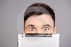 Close up portrait of young man hiding his face behind tablet