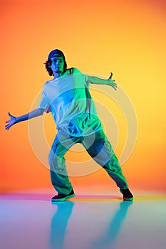 Close-up portrait of young man, hip-hop dancer in stylish clothes in action isolated on colorful background at dance