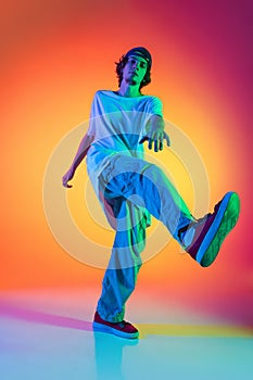 Close-up portrait of young man, hip-hop dancer in stylish clothes in action isolated on colorful background at dance