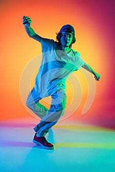 Close-up portrait of young man, hip-hop dancer in stylish clothes in action isolated on colorful background at dance