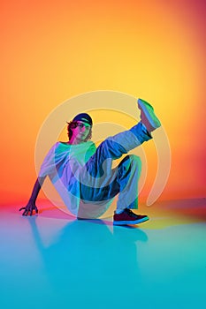 Close-up portrait of young man, hip-hop dancer in stylish clothes in action isolated on colorful background at dance