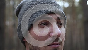 Close-up Portrait of a Young Man in a Knitted Hat on a Blurred Forest Background. Travel Concept, Hicking. Traveler On