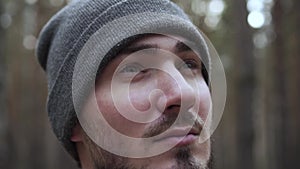 Close-up Portrait of a Young Man in a Knitted Hat on a Blurred Forest Background. Travel Concept, Hicking. Traveler On