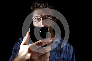 Close up portrait of young man looking intensively to mobile phone screen with blue eyes wide open isolated on black background photo