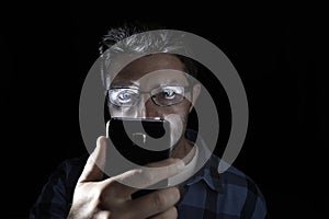 Close up portrait of young man looking intensively to mobile phone screen with blue eyes wide open isolated on black background photo