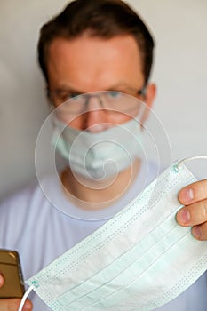 Close up portrait of young man putting on medical flu mask standing isolated on white background. Macro shot of man in