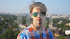 Close up portrait of young man in sunglasses sitting on rooftop of high-rise building with cityscape background