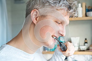 Close up portrait of Young Man is using electric ultrasound toothbrush. Male brushing teeth. Daily dental hygiene and