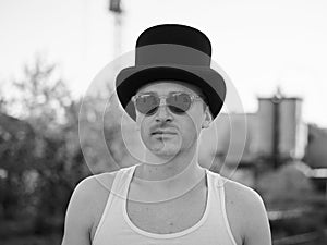 Three-quarter portrait of young man, wearing white top and black classic hat, holding sunglasses, smiling, laughing. Black and