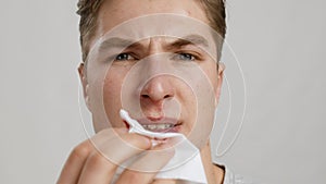 Close up portrait of young man wiping his bleeding nose with tissue, slow motion