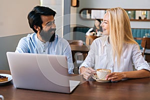 Close-up portrait of young man and woman sitting in restaurant and working on laptop. Attractive blonde female sitting