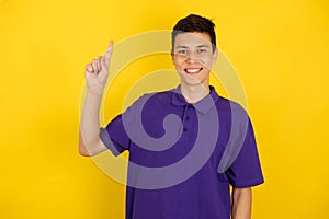 Close-up portrait of a young man on a yellow background, shows the index finger up, copy space