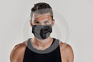 Close up portrait of young muscular caucasian man wearing black medical mask looking at camera while standing isolated