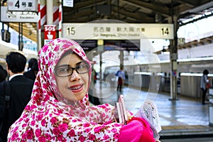 Close up portrait of young muslim woman wearing hijab on platform inside Kyoto train station with bokeh background.