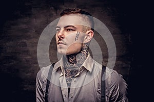 Close-up portrait of a young old-fashioned tattooed guy wearing white shirt and suspenders. on dark background.