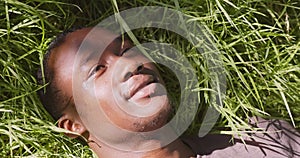 Close up portrait of young peaceful african american man lying on green grass, relaxing and enjoying summer wind