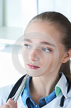 Close-up portrait of young pensive doctor in white uniform sitting at her workplace. Medical consultant, nurse