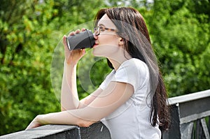 Close-up portrait young pretty woman drinking coffee from black paper cup sitting on a bridge in the park