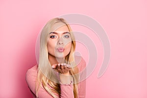 Close up portrait of young pretty woman sending kiss to the camera, standing over pink background