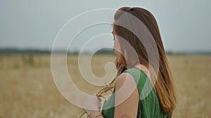 Close-up portrait. Young red-haired woman in a green dress in an evening wheat field. Golden field of ripe wheat. Slow