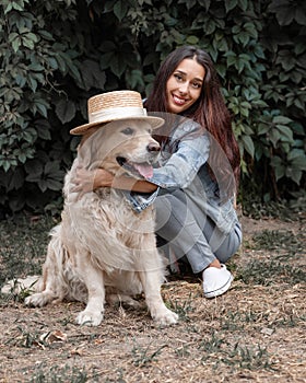 Close-up portrait of young smiling 25-30 years old woman embraces her cute dog golden retriever labrador in summer park.