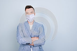 Close up portrait of young successful guy with crossed arms wearing white face mask isolated on grey colored background