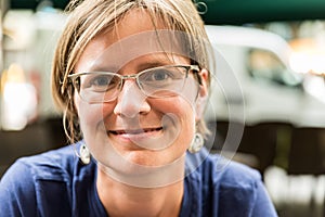 Close up portrait of a young white woman with glasses wearing a blue and sweather with a bokeh city background