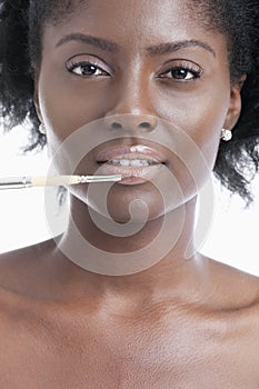 Close-up portrait of young woman applying lip gloss with brush