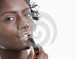 Close-up portrait of young woman applying lipstick over white background