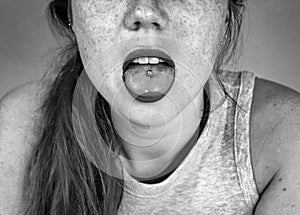Close up portrait of young woman sticking out pierced tongue, showing her tongue piercing black and white