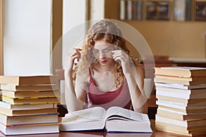 Close up portrait of young woman touching her eyeglasses, reading paper book. Female student spending long hours, wearing glasses