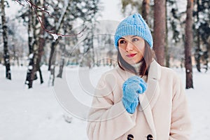 Close up portrait of young woman walking under snowfall in winter park wearing white fur coat blue hat mittens