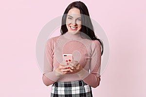 Close up portraite of cute Caucasian woman using smart phone for texting or chatting with her friend, hearing funny news, laughing