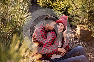 Close-up portraits of young couple in red checkered shirts sitting among Christmas tree seedlings