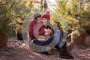 Close-up portraits of young couple in red checkered shirts sitting among Christmas tree seedlings