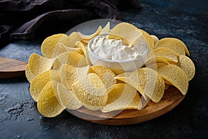 Close-up potato chips and sauce in a white bowl on a wooden cutting board