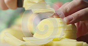 Close up of Potato Slicing with a Knife to Cook French Fries with Vegetables on the Background